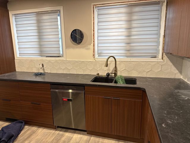 Kitchen sink area with two windows, dark wood cabinets, and a stainless dishwasher under the counter