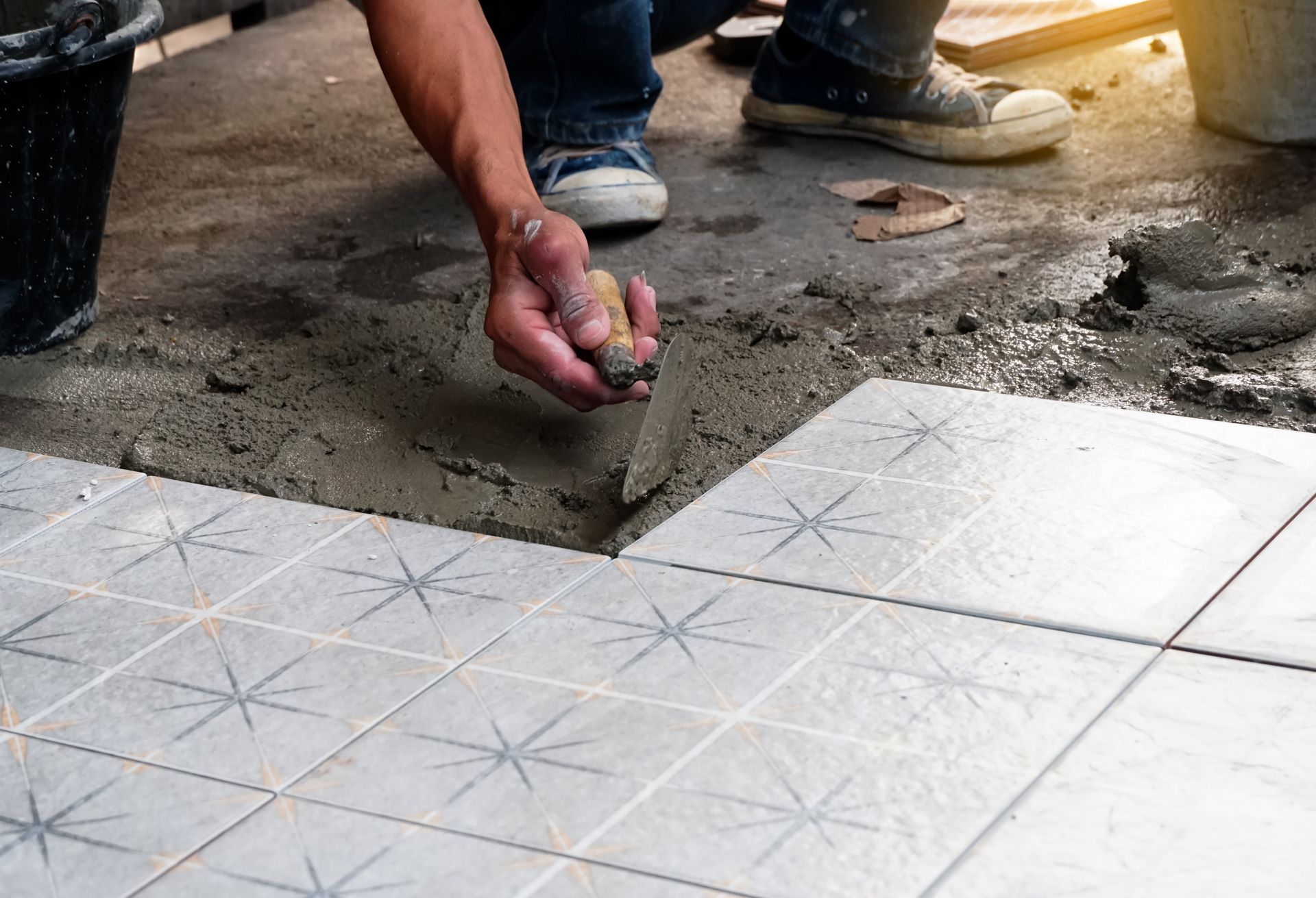 Worker hand places a tile spacer while installing patterned white floor tiles outdoors