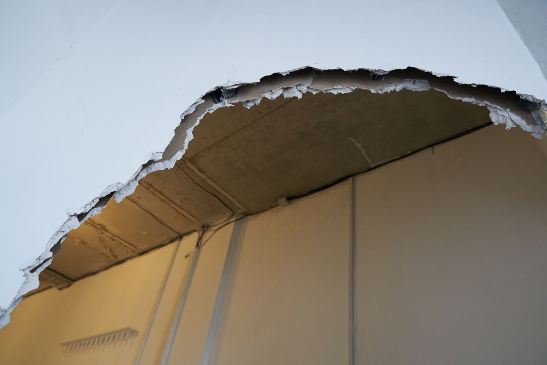 Damaged ceiling with a large hole exposing torn drywall and insulation