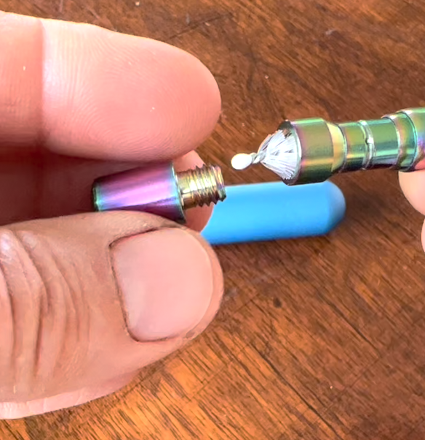 A person is holding a rainbow colored pen on a wooden table.