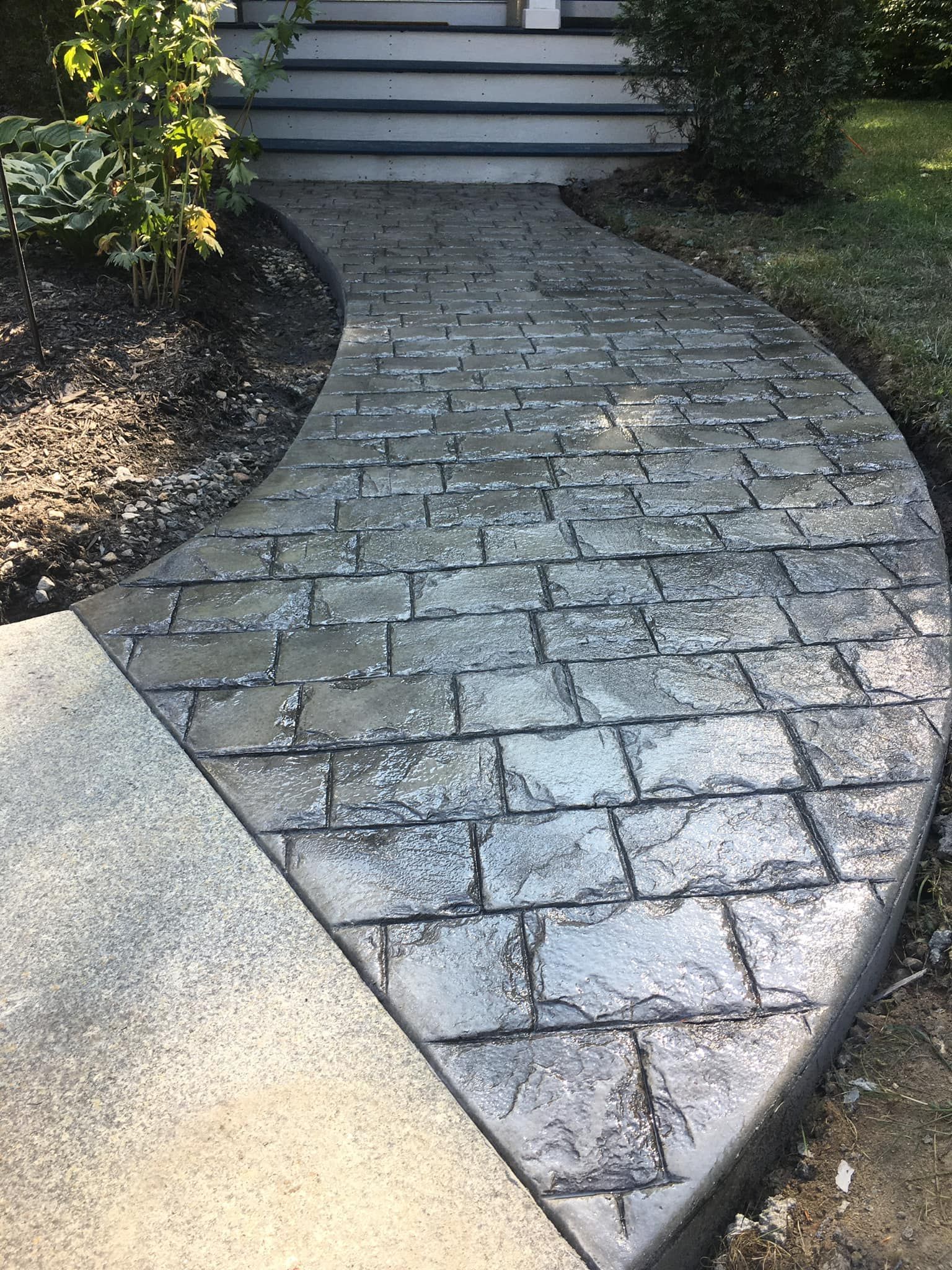 A curved brick walkway leading to a house with stairs.