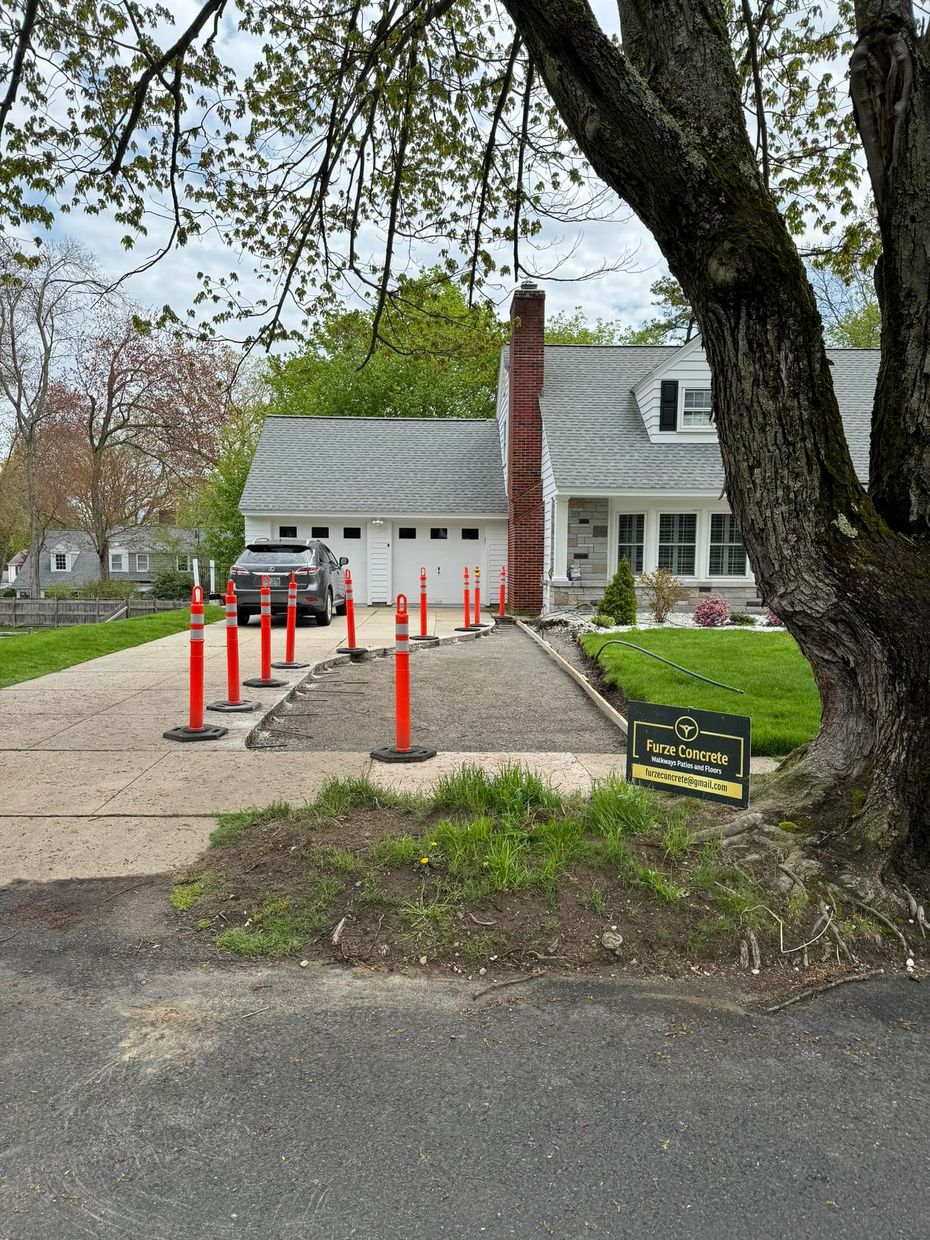 A car is parked in a driveway next to a tree.