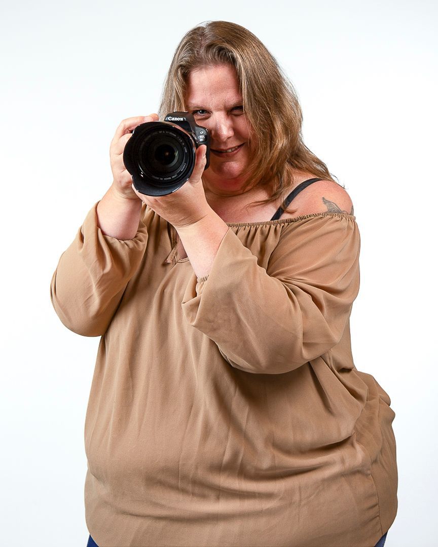 Vrouw kijkt door de cameralens, gekleed in een beige shirt.