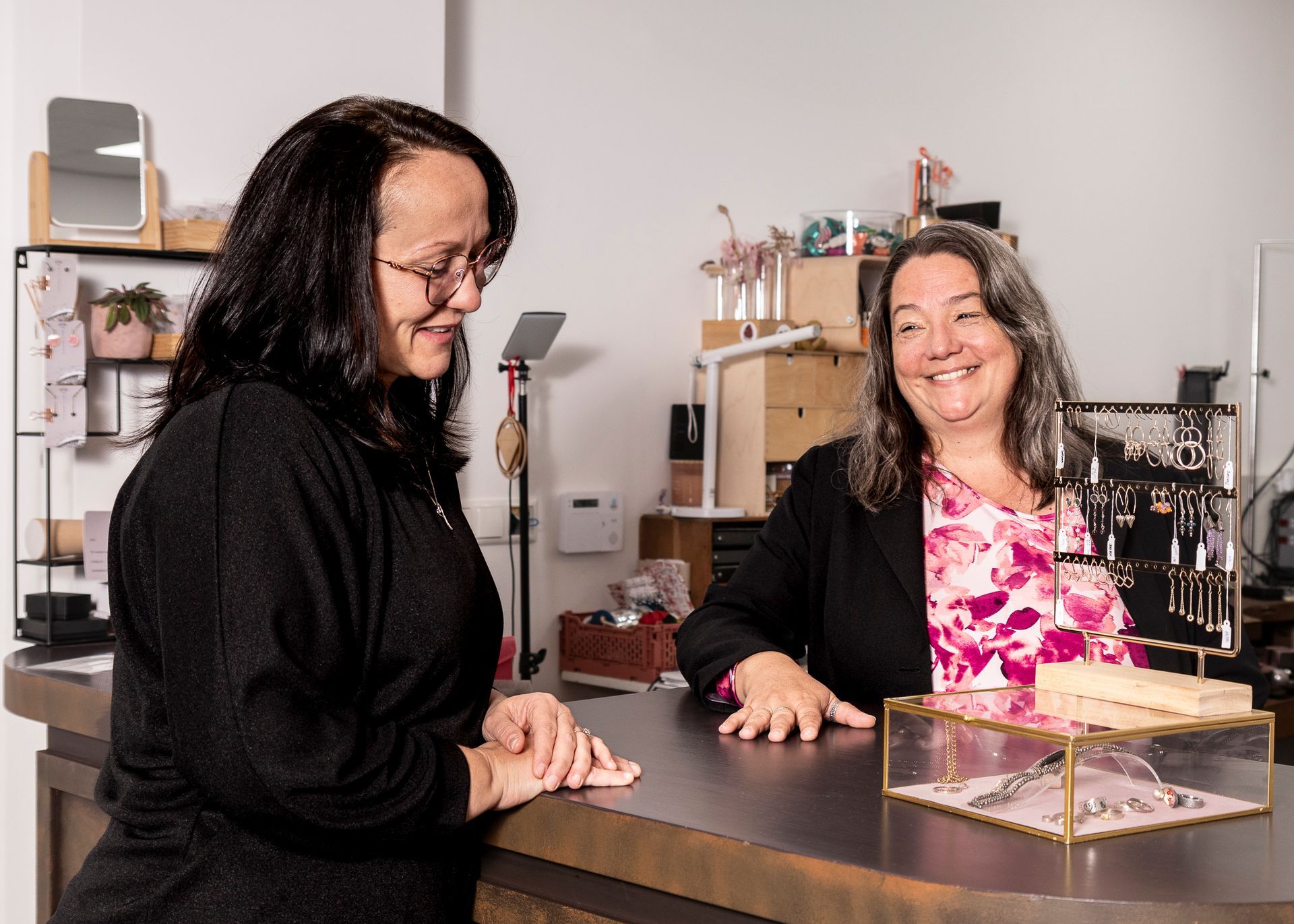 Vrouw staat bij de toonbank van een juwelierszaak en kijkt naar de vitrine, terwijl de eigenaresse van de winkel glimlacht.
