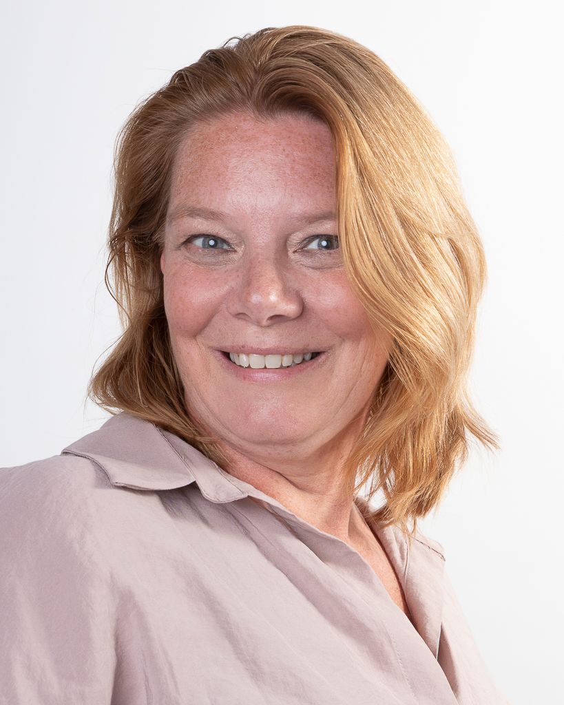 Een vrouw met lichtbruin haar, gekleed in een lichtroze shirt, lacht tegen een witte achtergrond.