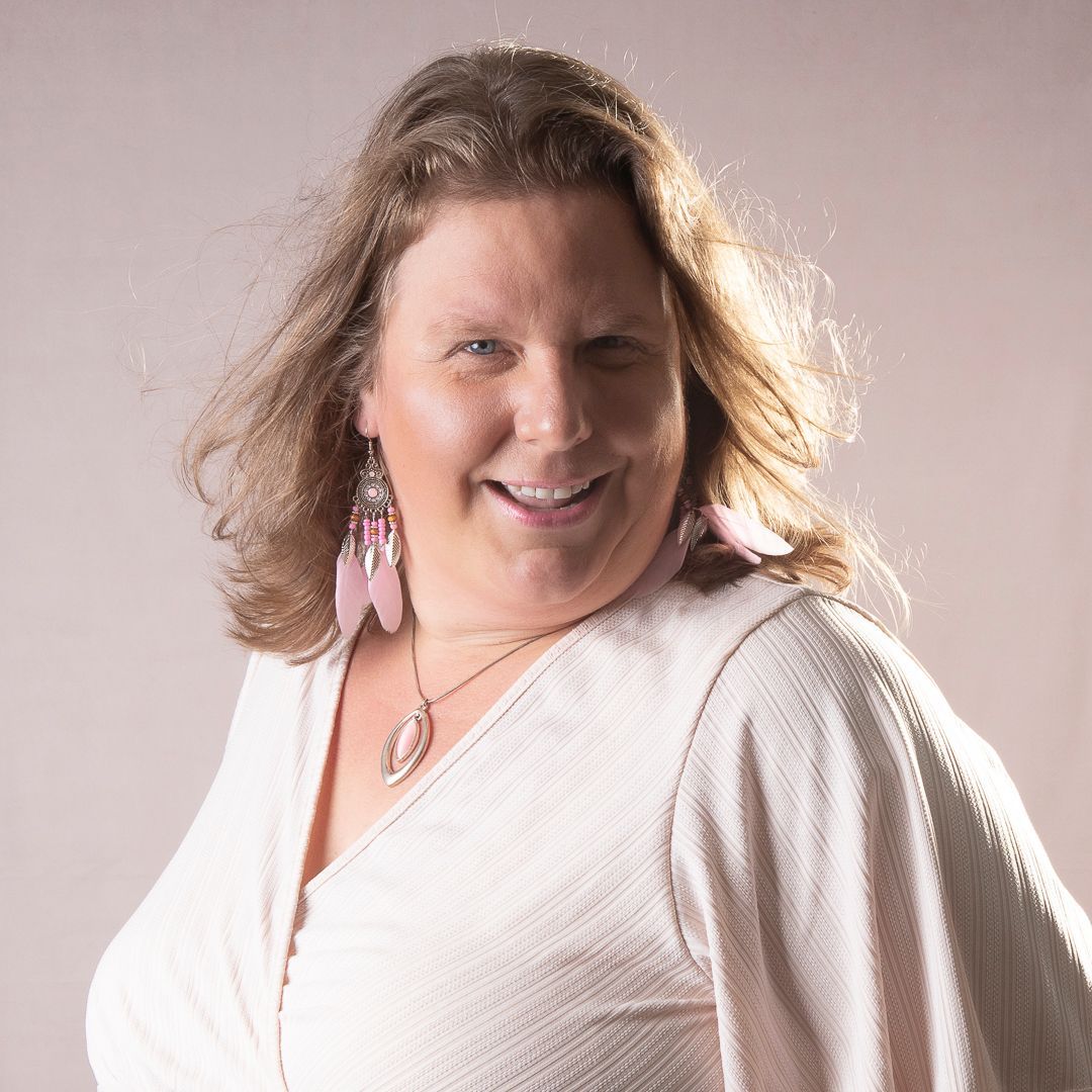 Vrouw in witte top, lachend, met roze oorbellen, kijkt naar de camera. Studio-opname.