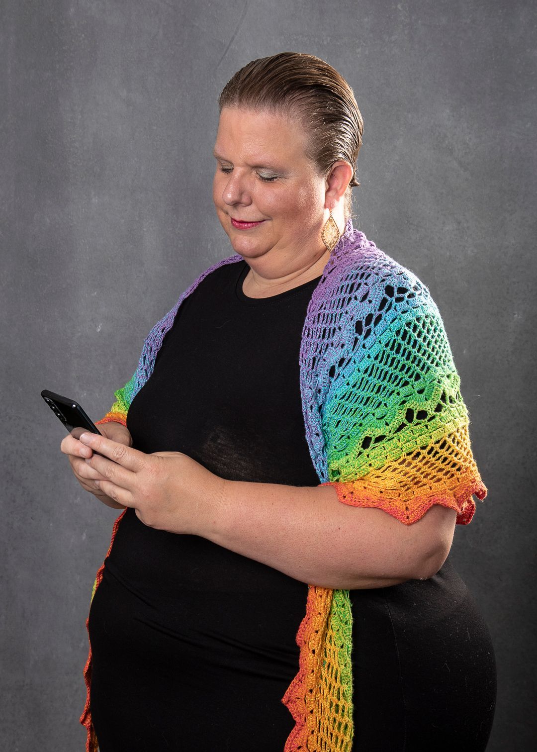 klik hier Vrouw in zwarte jurk, gehaakte regenboogsjaal, kijkt naar haar telefoon. Grijze achtergrond. Make a Change Call