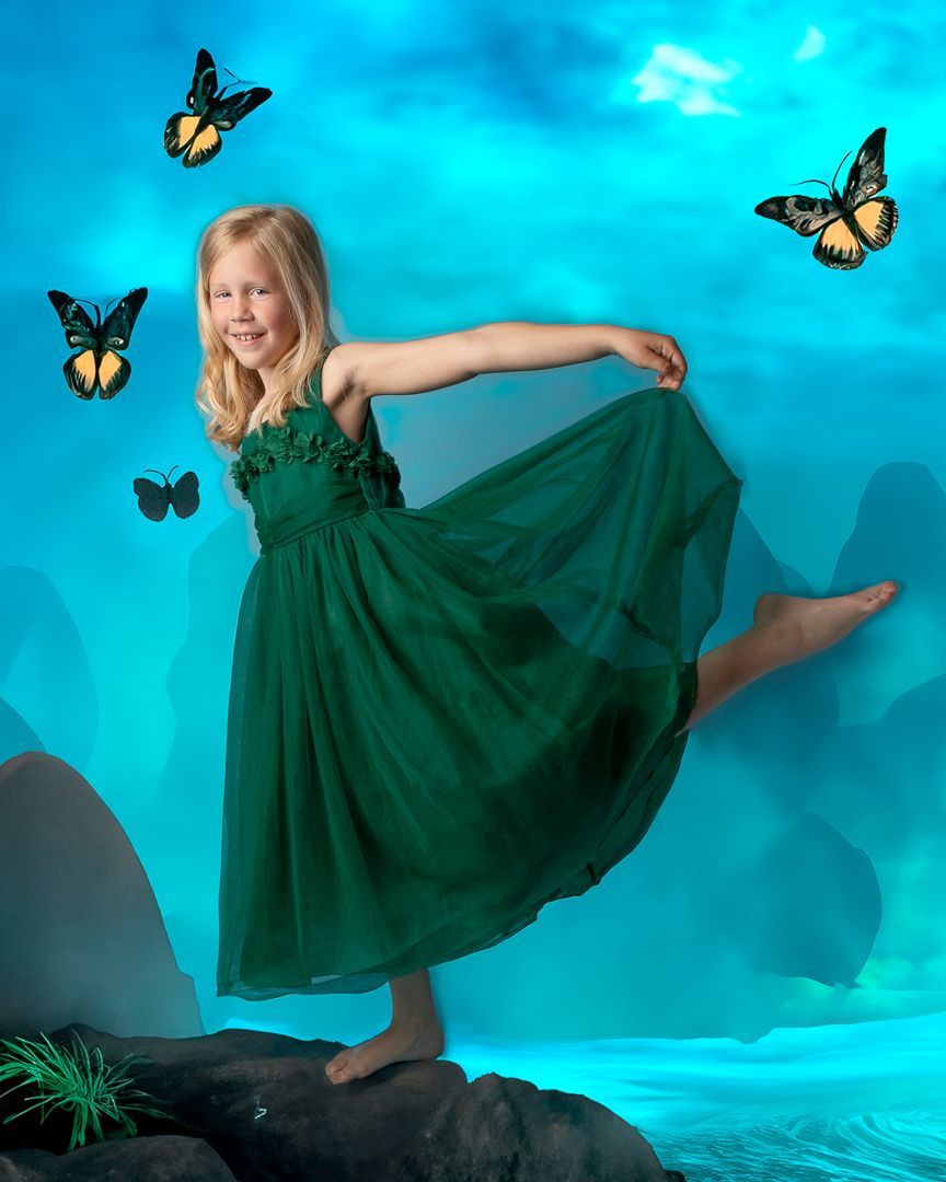 Een jong meisje in een groene jurk poseert op een rots, omringd door vlinders, tegen een blauwe achtergrond.
