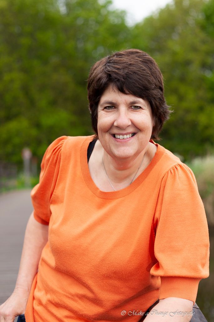Vrouw in oranje top lacht buiten tegen een groene achtergrond.