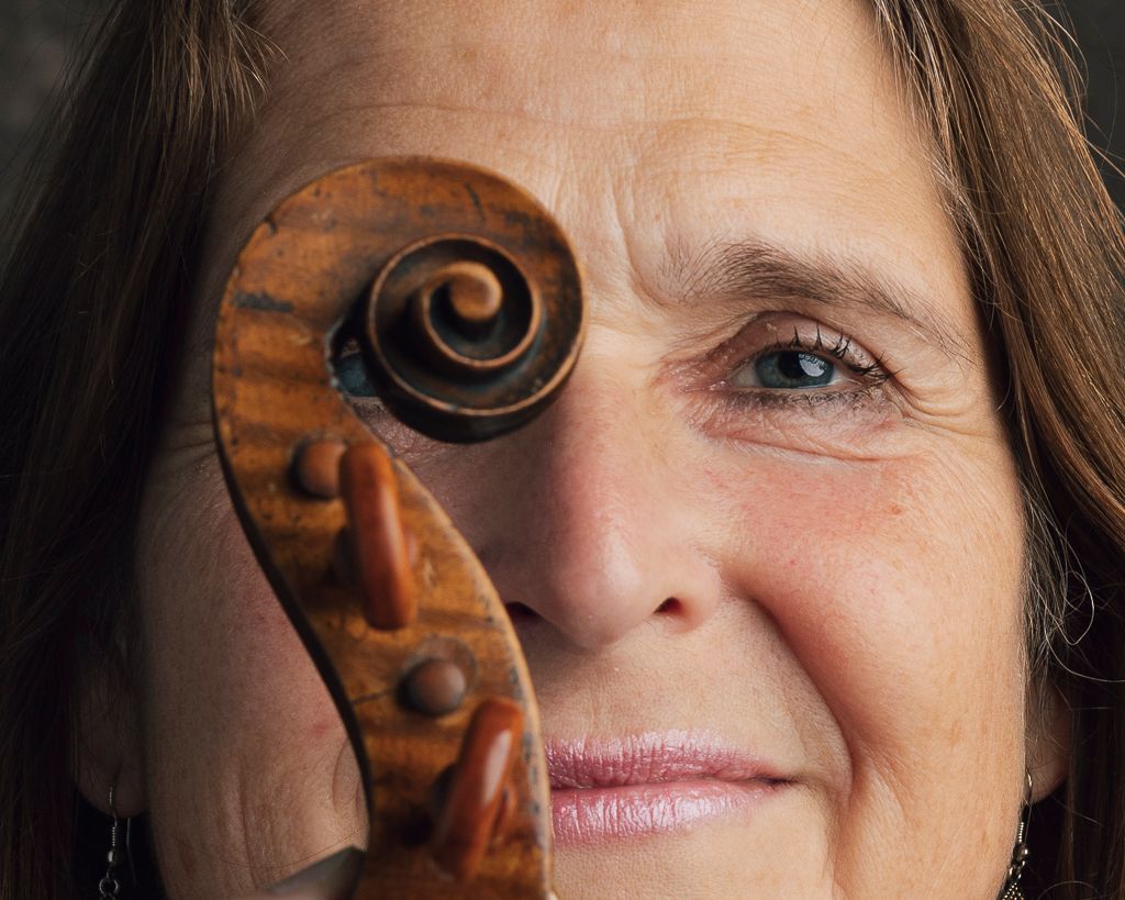 Het oog van een vrouw dat door de krul van een viool heen gluurt; warme tinten; close-up.