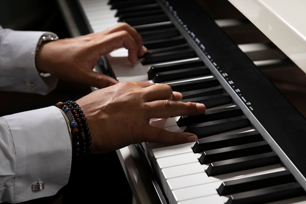 Handen die piano spelen, gekleed in een wit shirt en met kralenarmbanden, op een klavier met zwarte en witte toetsen.