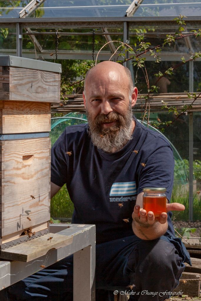 Imker met pot honing bij bijenkorf in zonnige tuin.