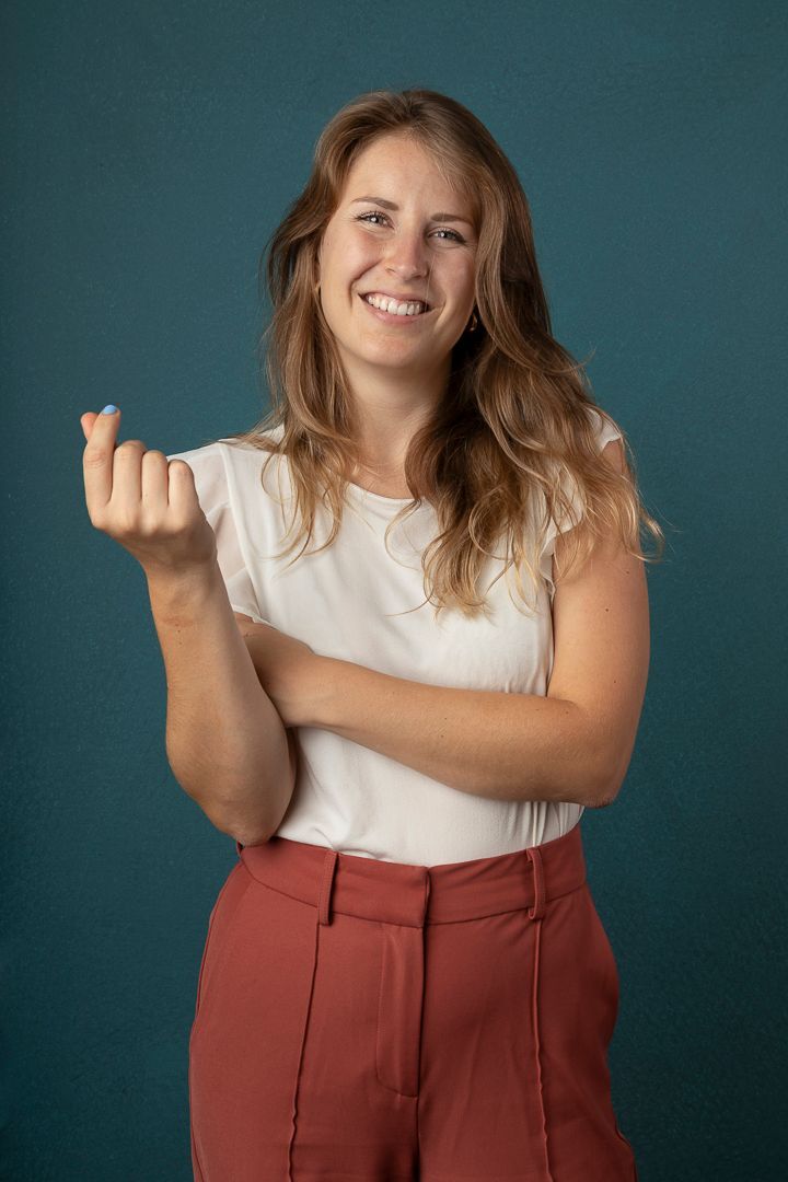 Een vrouw glimlacht en maakt een geld beweging met haar vingers, tegen een turquoise achtergrond.