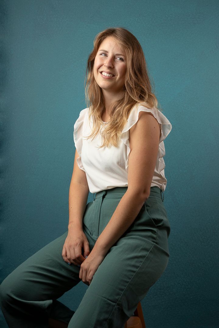 Een lachende vrouw zit met haar handen ineengevouwen, tegen een turquoise achtergrond.