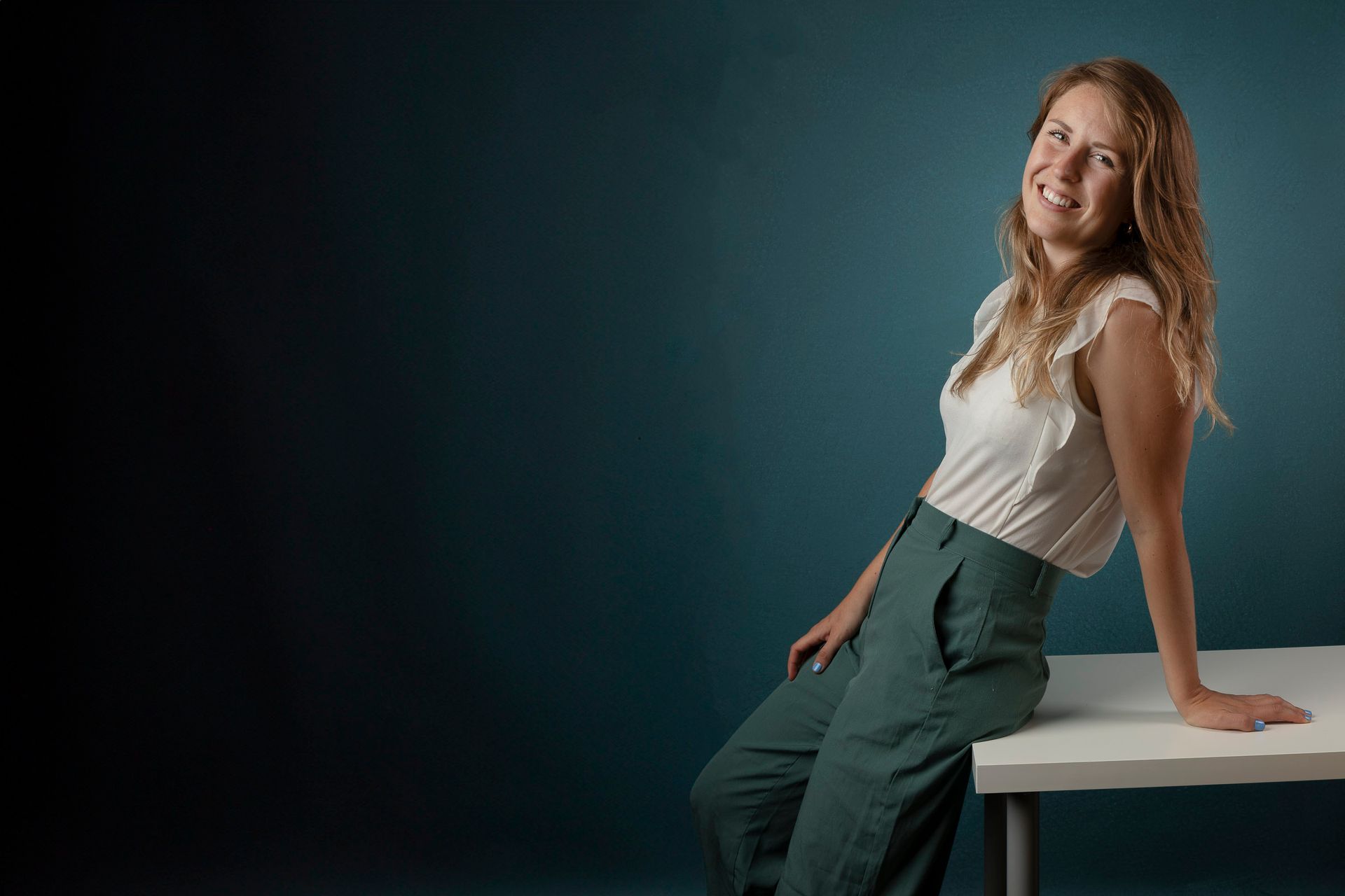 Een vrouw glimlacht en leunt tegen een witte tafel. tegen een blauwe achtergrond.