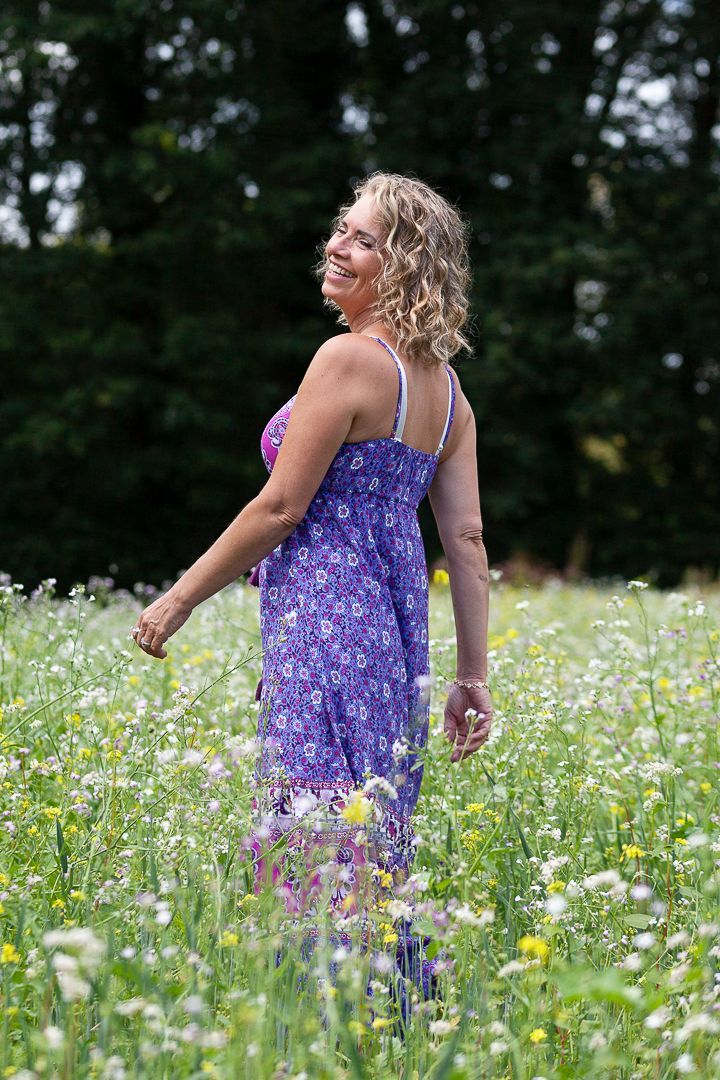 Vrouw in paarse jurk loopt in een veld vol wilde bloemen; ze lacht.