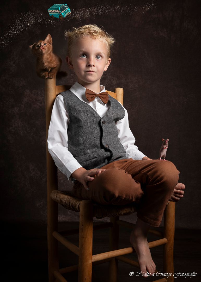 Een jongen in een vest en vlinderdas zit op een stoel; speelgoed dwarrelt om hem heen tegen een donkere achtergrond.