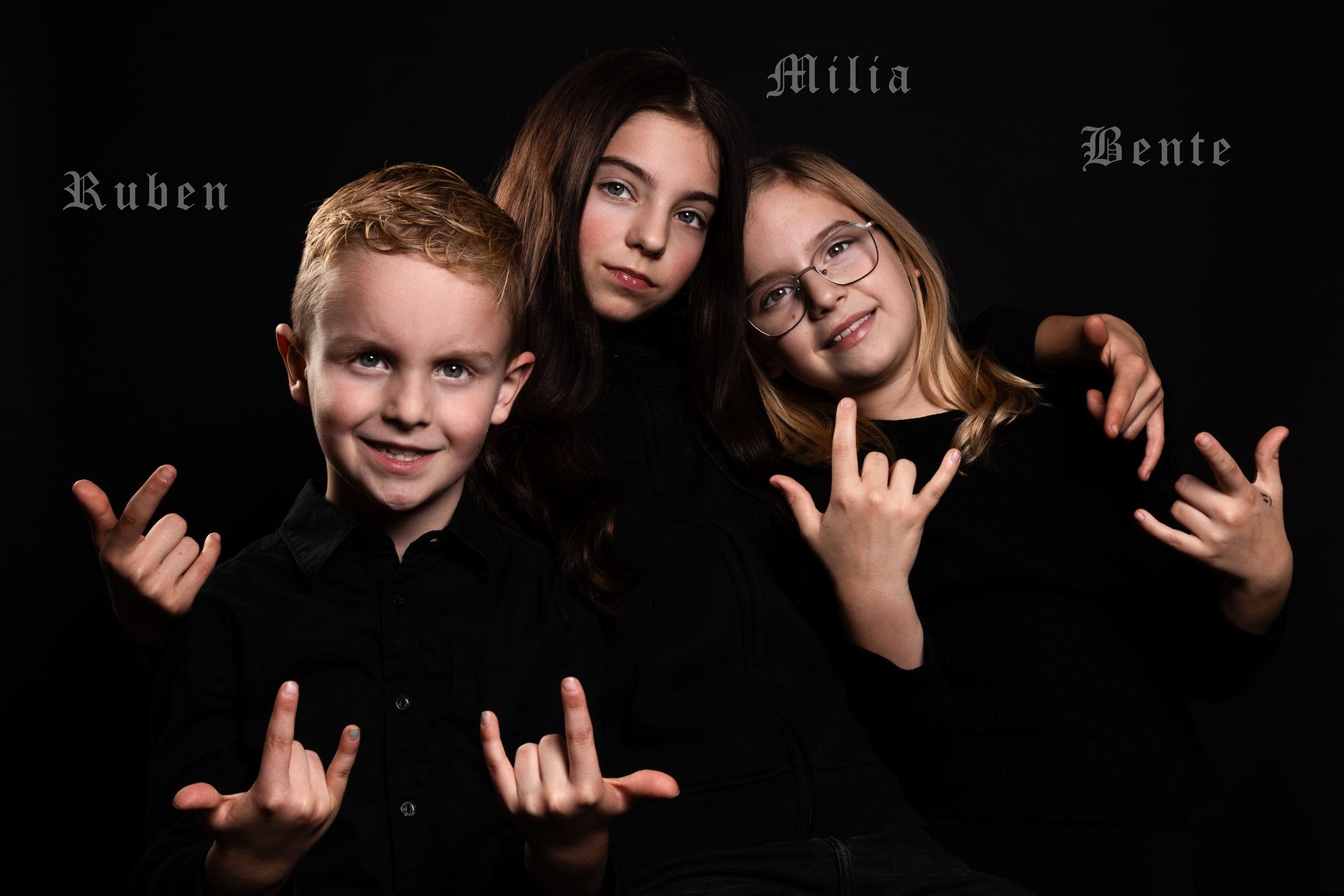 Drie mensen in zwarte kleding maken een rock-'n-roll-handgebaar tegen een zwarte achtergrond.