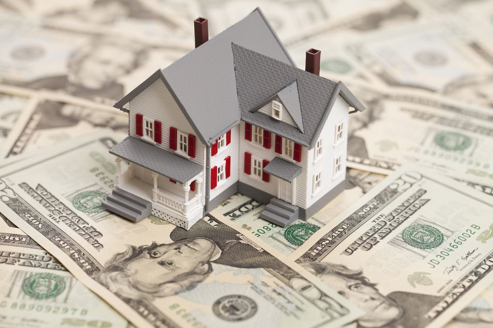 Miniature house model on U.S. dollar bills, suggesting home financing or real estate investment