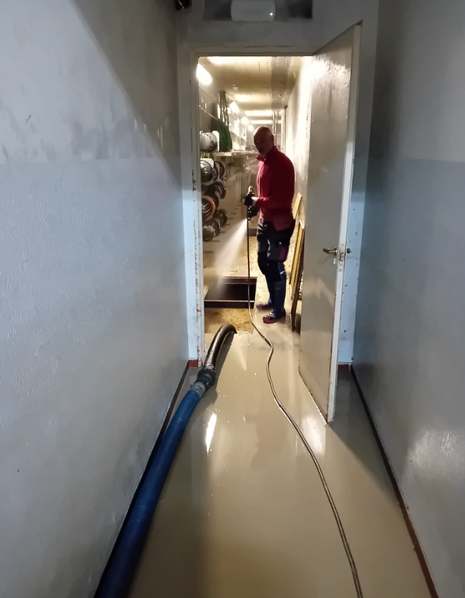 Una persona con una maglietta rossa è in piedi in uno stretto corridoio accanto a un tubo blu sul pavimento.