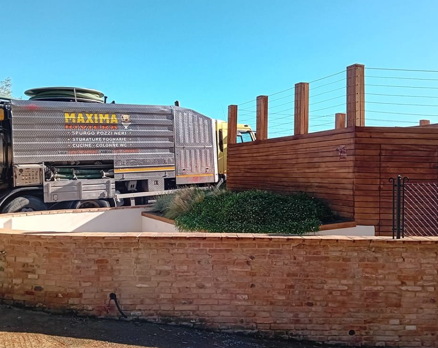 Camion parcheggiato accanto a un muro di mattoni, vicino a un edificio di legno, sotto un cielo azzurro.