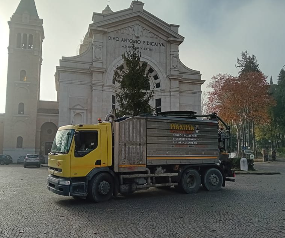 Un camion giallo da carico è parcheggiato davanti a una grande chiesa in una piazza lastricata e nebbiosa.