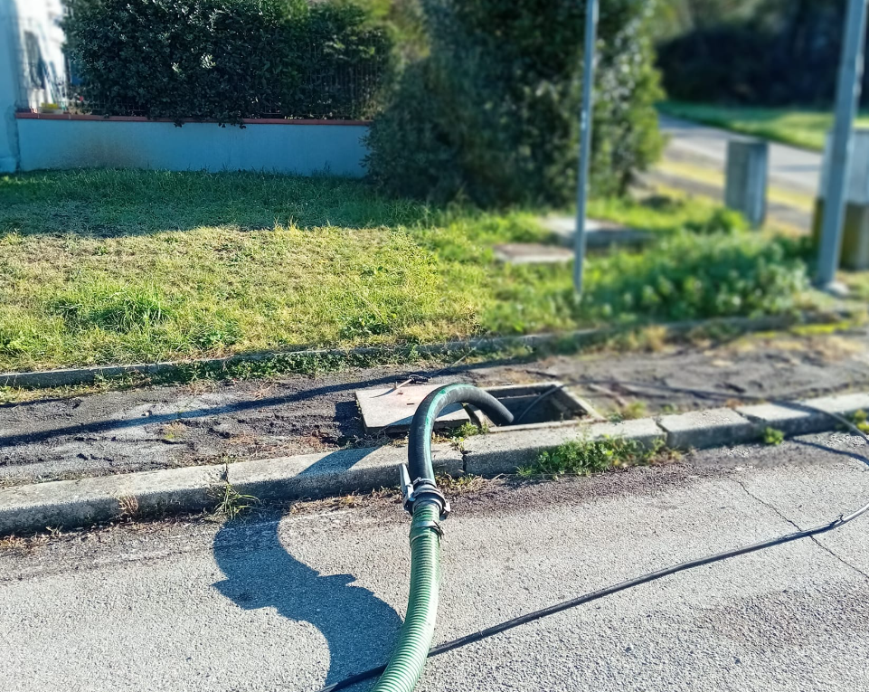 Un tubo verde scarica in una griglia di scolo stradale accanto al marciapiede, con erba e marciapiede nelle vicinanze.