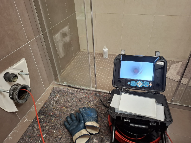 Telecamera di ispezione dell'idraulico posizionata sul pavimento del bagno, accanto a tubi e scarico, con guanti nelle vicinanze.