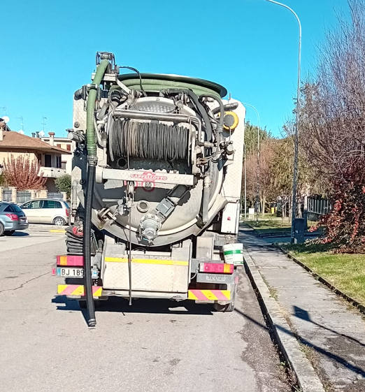 Camion della nettezza urbana parcheggiato in una soleggiata strada residenziale, con tubi posteriori e attrezzature ben visibili.