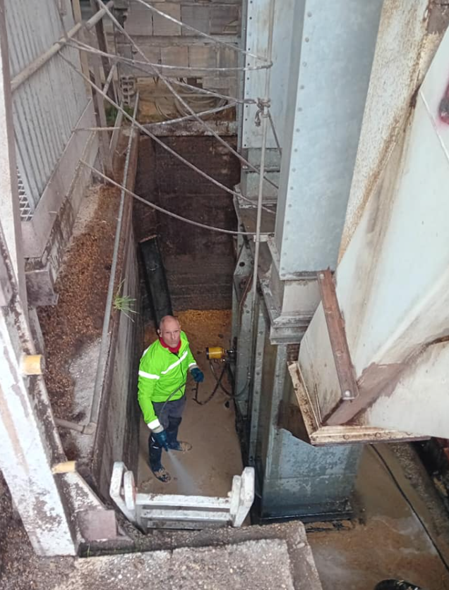 Un operaio con una giacca verde neon è in piedi in una stretta trincea industriale sotto un'impalcatura.