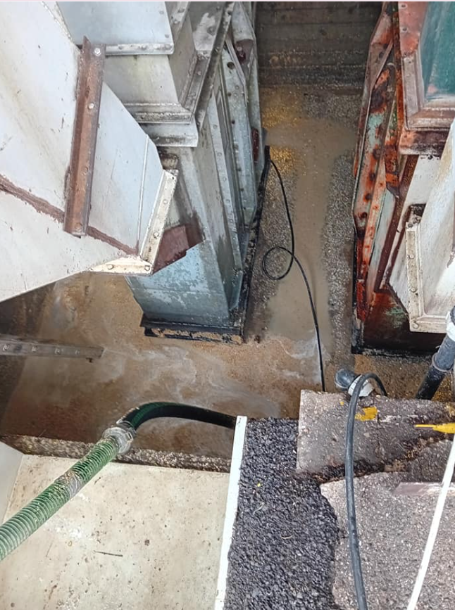 Stretto pozzo di costruzione con tubi, cavi e pareti in cemento a vista, al di sotto di un bordo di ghiaia.