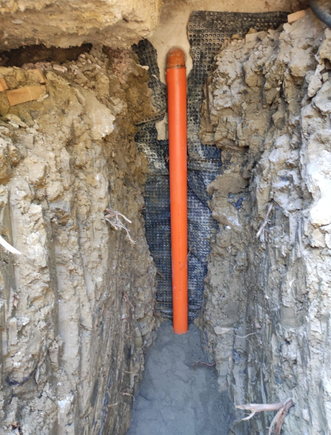 Tubo arancione in una stretta trincea di terra accanto a muri di cemento grezzo.