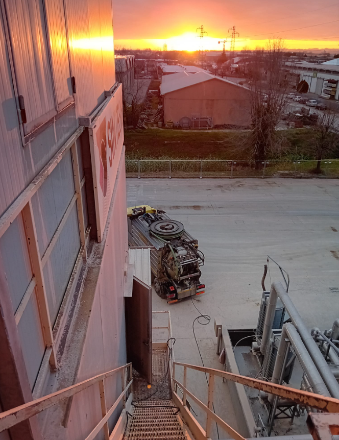 L'alba su un'area industriale, vista da una scala metallica accanto a tubi e un camion.