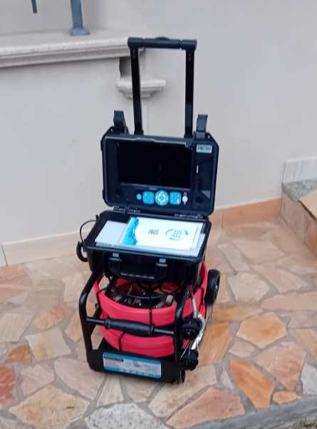 Carrello nero con ruote, schermo e tablet montati frontalmente, posizionato all'interno su un pavimento piastrellato.