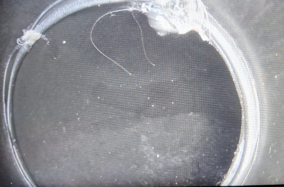Primo piano dell'apertura di un anello o tubo di plastica bianca con interno scuro e trama a rete.