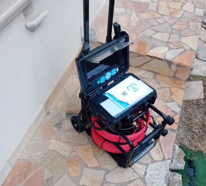 Carrello di ispezione portatile con monitor e cavo rosso arrotolato su un portico piastrellato all'aperto.
