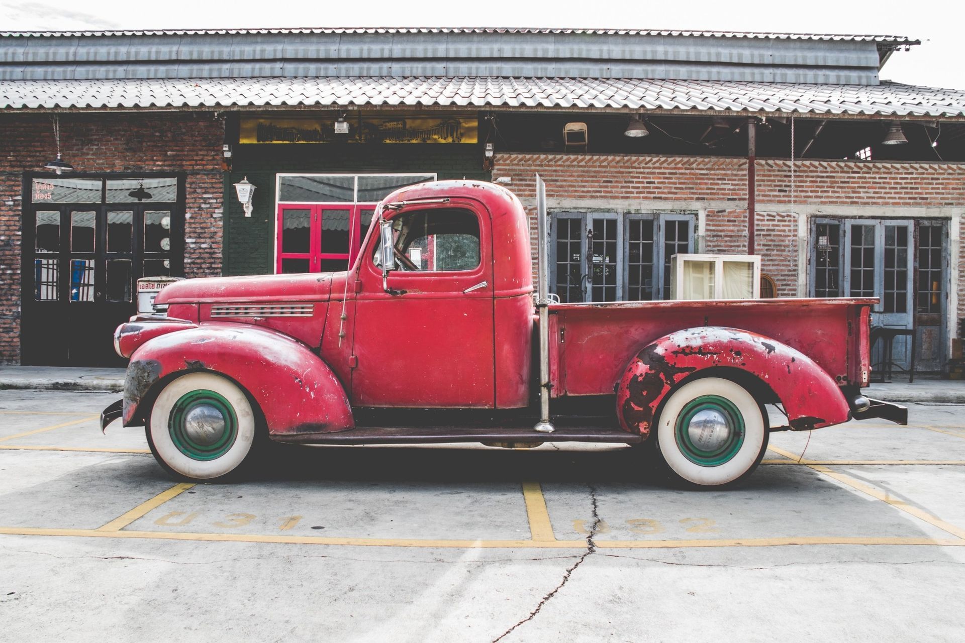 Vintage red pickup truck parked on a street in front of a brick building.
