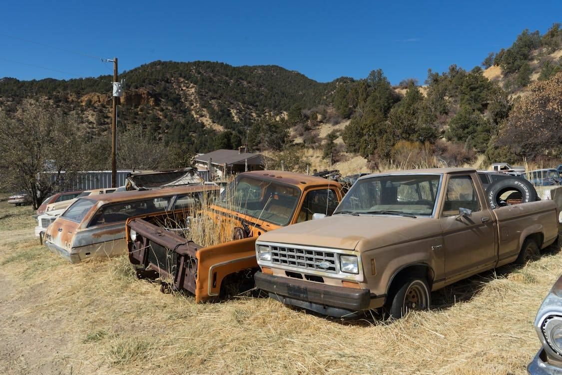 Several rusty old pickup trucks parked in a dry field with hills in the background
