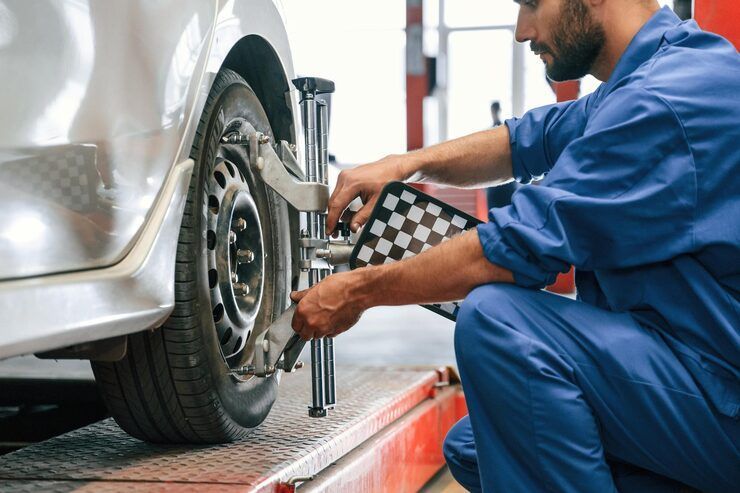Mechanic in blue overalls adjusting car tire alignment with a checkered pattern tool in a garage.