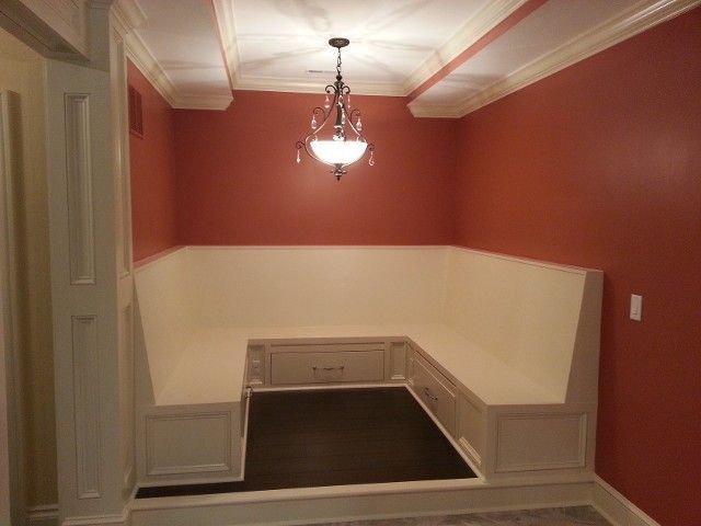 U-shaped built-in bench seating with white cabinetry and dark wood floors, illuminated by a hanging chandelier.