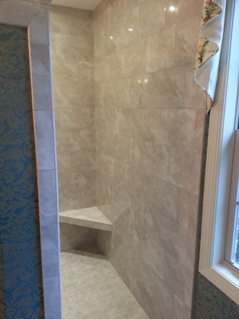 A tiled shower stall featuring beige wall tiles, a built-in corner seat, and a decorative blue patterned accent wall.