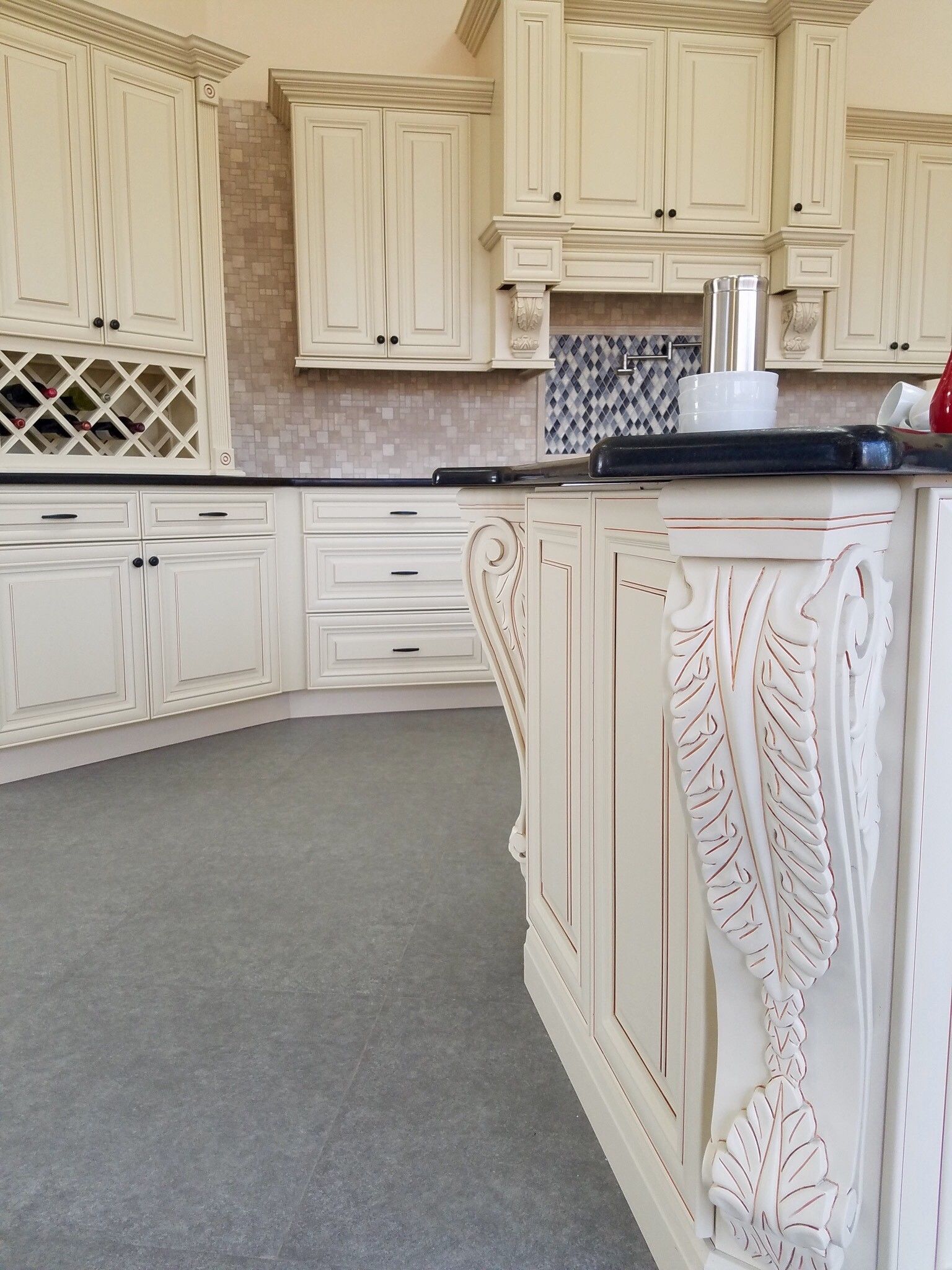 Cream-colored kitchen cabinets with decorative wood carvings, ornate detailing, and dark countertops.