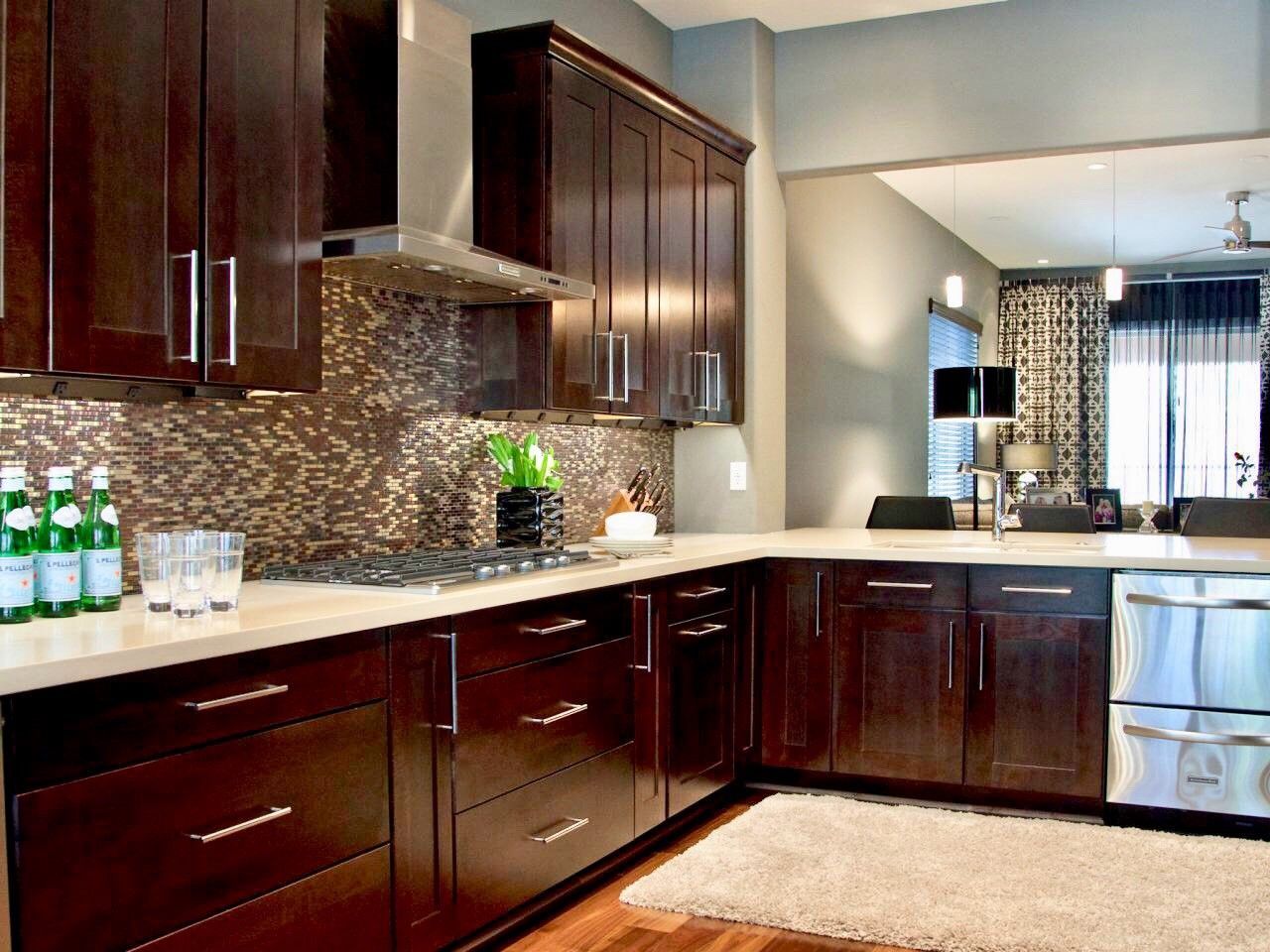 Modern kitchen with dark wood cabinets, stainless steel appliances, light countertops, and a textured backsplash.