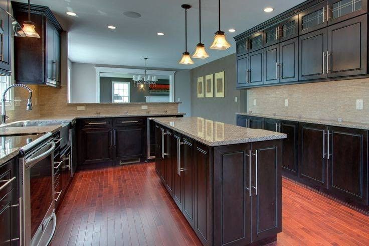 Modern kitchen with dark wood cabinets, light granite countertops, stainless steel appliances, and wood flooring.