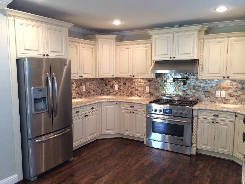 A modern kitchen featuring off-white raised-panel cabinets, stainless steel appliances, and a tiled mosaic backsplash.