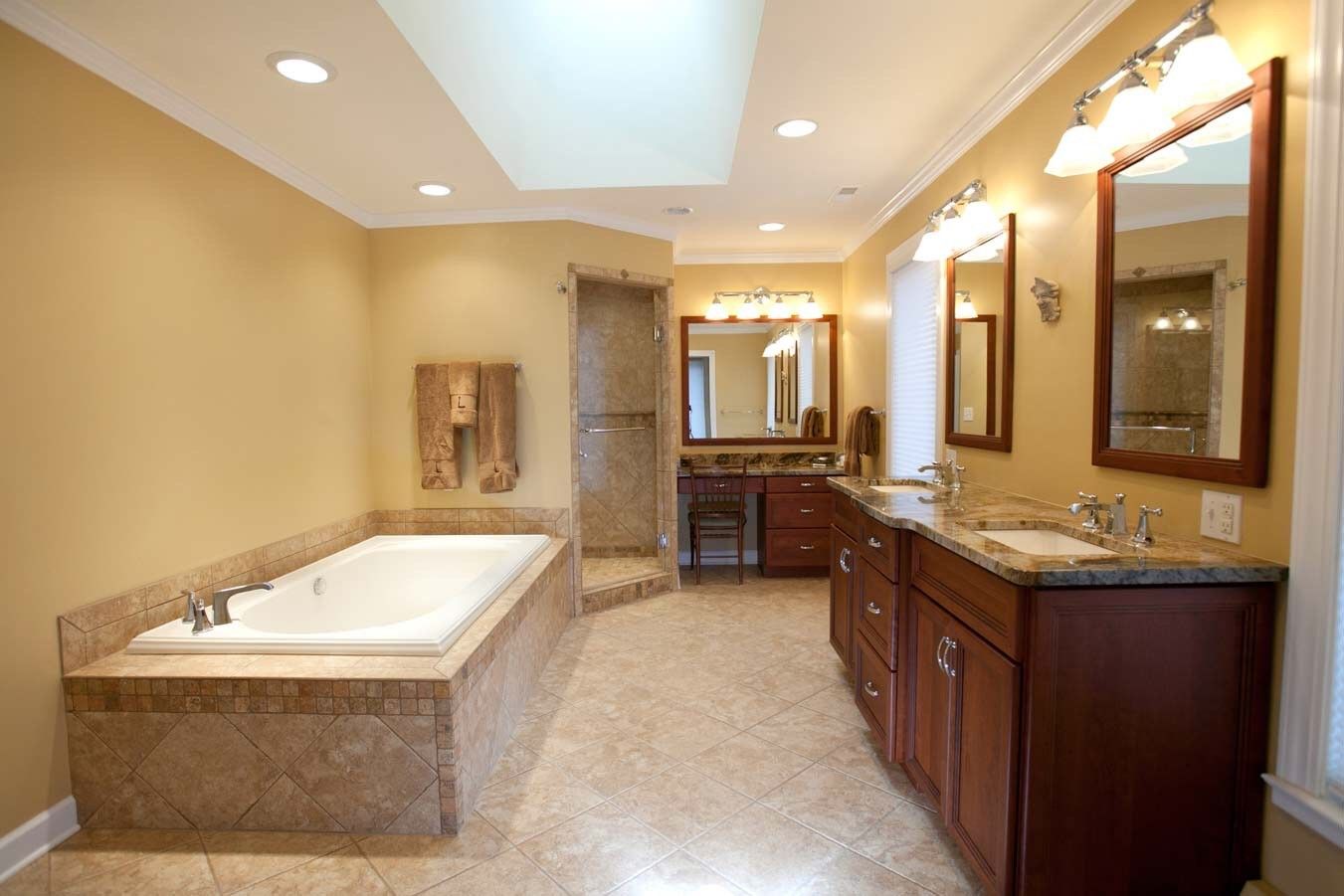 A spacious bathroom with a large tiled bathtub, a dual-sink vanity with wood cabinets, and a glass-enclosed shower.