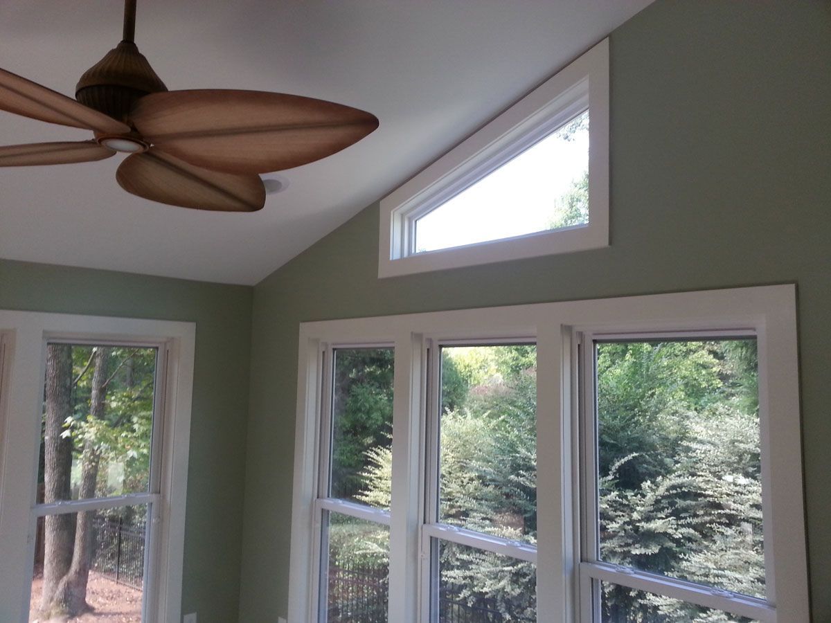 A sunroom corner with sage green walls, large windows, a triangular transom window, and a leaf-shaped ceiling fan.