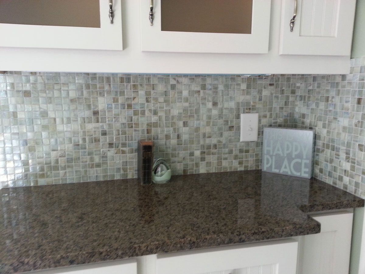 Brown granite countertop with a multi-colored glass mosaic tile backsplash and white cabinets in a kitchen.