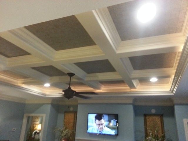 A living room with a coffered ceiling featuring dark panels, recessed lighting, and a ceiling fan over a television wall.
