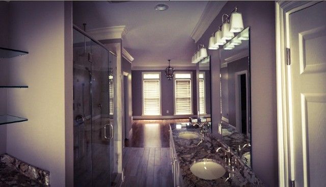 A modern bathroom featuring a glass shower, dual vanity with a granite countertop, and a large mirror with warm lighting.